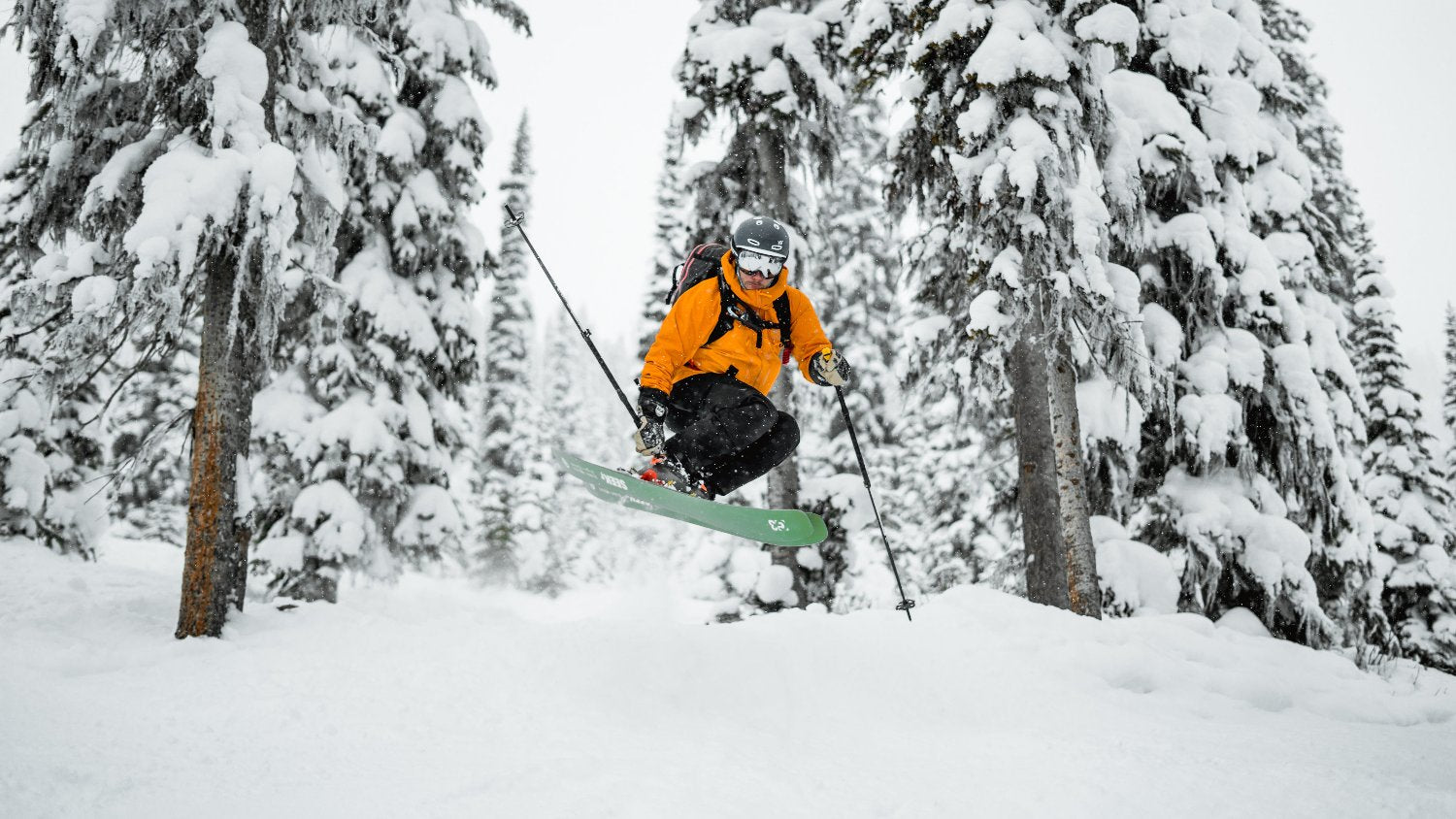 skier in air surrounded by snow covered trees